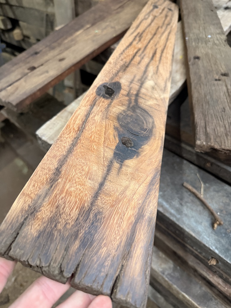 A reclaimed ulin plank held in a hand, weathered grey on the outside and warm brown where it has been planed